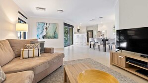 A modern living room with a sofa, coffee table, TV, and dining area. - Surfside 1—An Unforgettable Yallingup Experience (Yallingup)