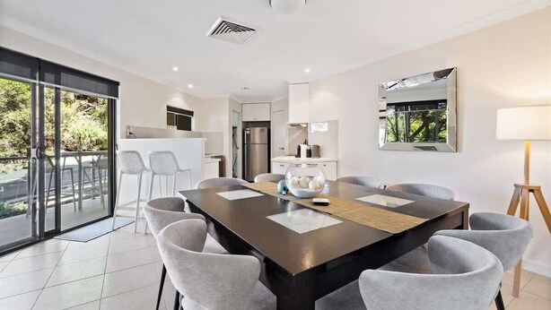 A modern dining area with a large table, chairs, and a view through glass doors to an outdoor space. - Surfside 1—An Unforgettable Yallingup Experience (Yallingup)