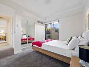 A modern bedroom with a large bed, a sliding glass door to a balcony, and a separate room visible through the door.