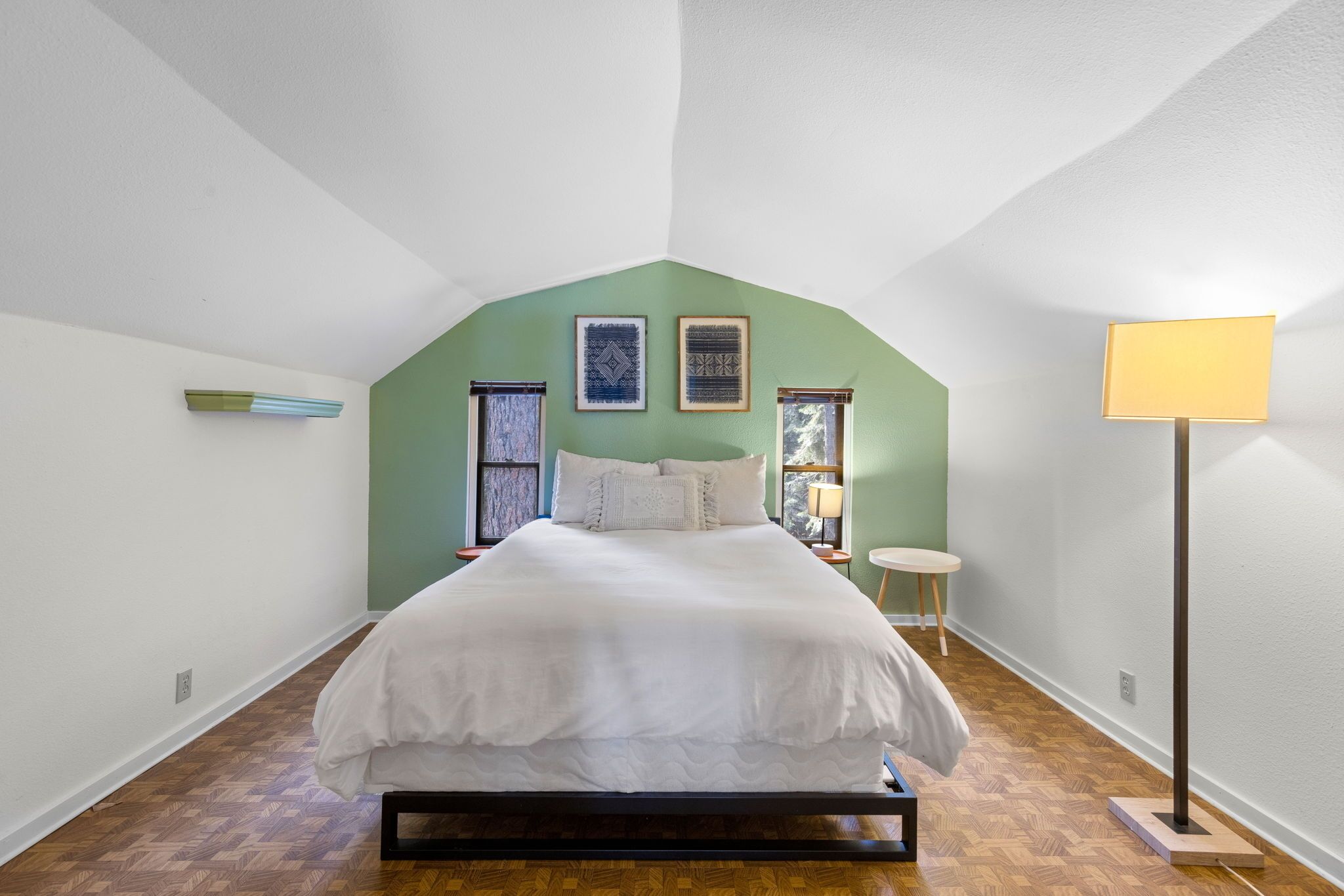 A bedroom with a bed, a floor lamp, and two framed pictures on the wall.
