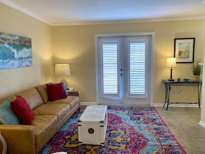 A living room with a beige sofa, colorful rug, and a white wicker coffee table.