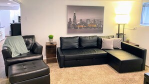 A modern living room with a black leather sofa, a matching ottoman, and a cityscape painting on the wall.