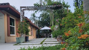 Un sendero en un jardín que lleva a una casa con una pérgola y plantas en macetas.