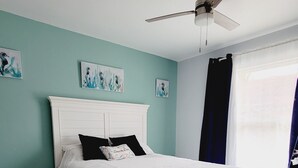 Un dormitorio con cama blanca, paredes verde azulado y obras de arte.
