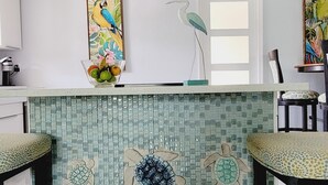 Una cocina con salpicadero de azulejos con motivos marinos, una isla central con taburetes y una ventana sobre el fregadero.
