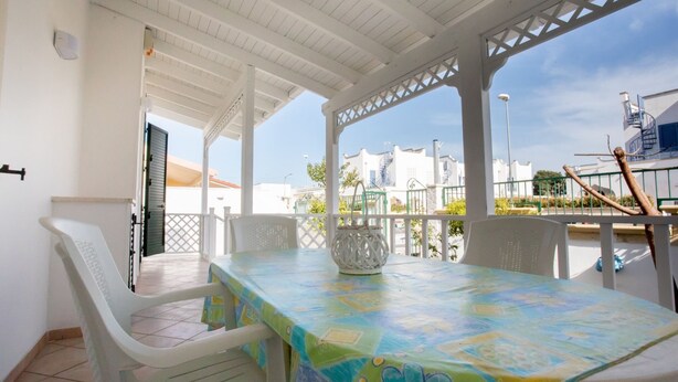 Een terras buiten met een tafel en stoelen, een pergola, en gebouwen op de achtergrond.