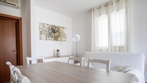 Een eetruimte met een houten tafel, witte stoelen, een schilderij aan de muur en een radiator.
