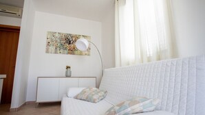 Een slaapkamer met een wit bed, een nachtkastje met een vaas, een wandlamp en een schilderij.