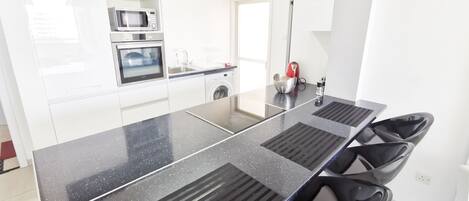 A modern kitchen with a black granite countertop, stainless steel appliances, and black chairs.