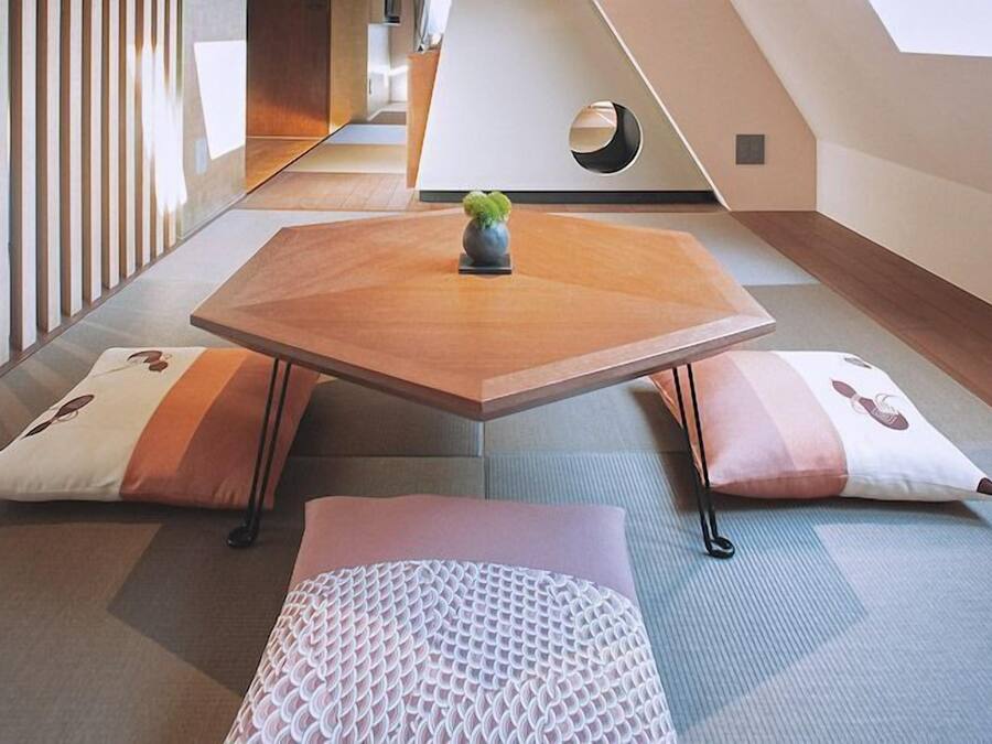 A modern, minimalist room with a tatami mat floor, a low wooden table, and two cushions with a geometric pattern.