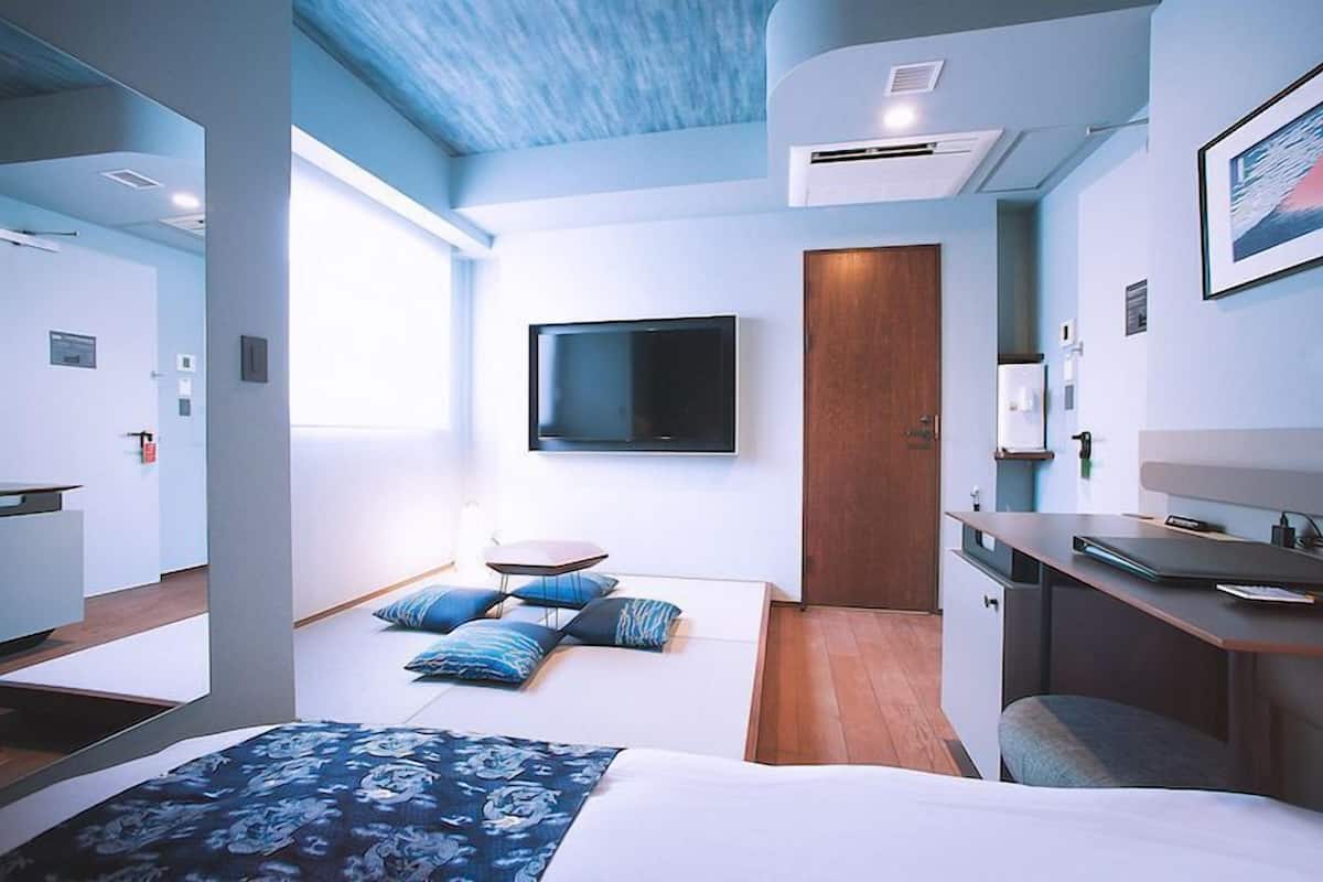 Quarto de hotel moderno com cama, escrivaninha, TV de tela plana e porta.