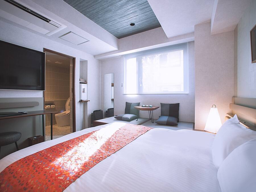 Une chambre d’hôtel dotée d’un grand lit, d’un bureau avec un téléviseur à écran plat, d’une petite table avec des chaises et d’une fenêtre laissant entrer la lumière naturelle.