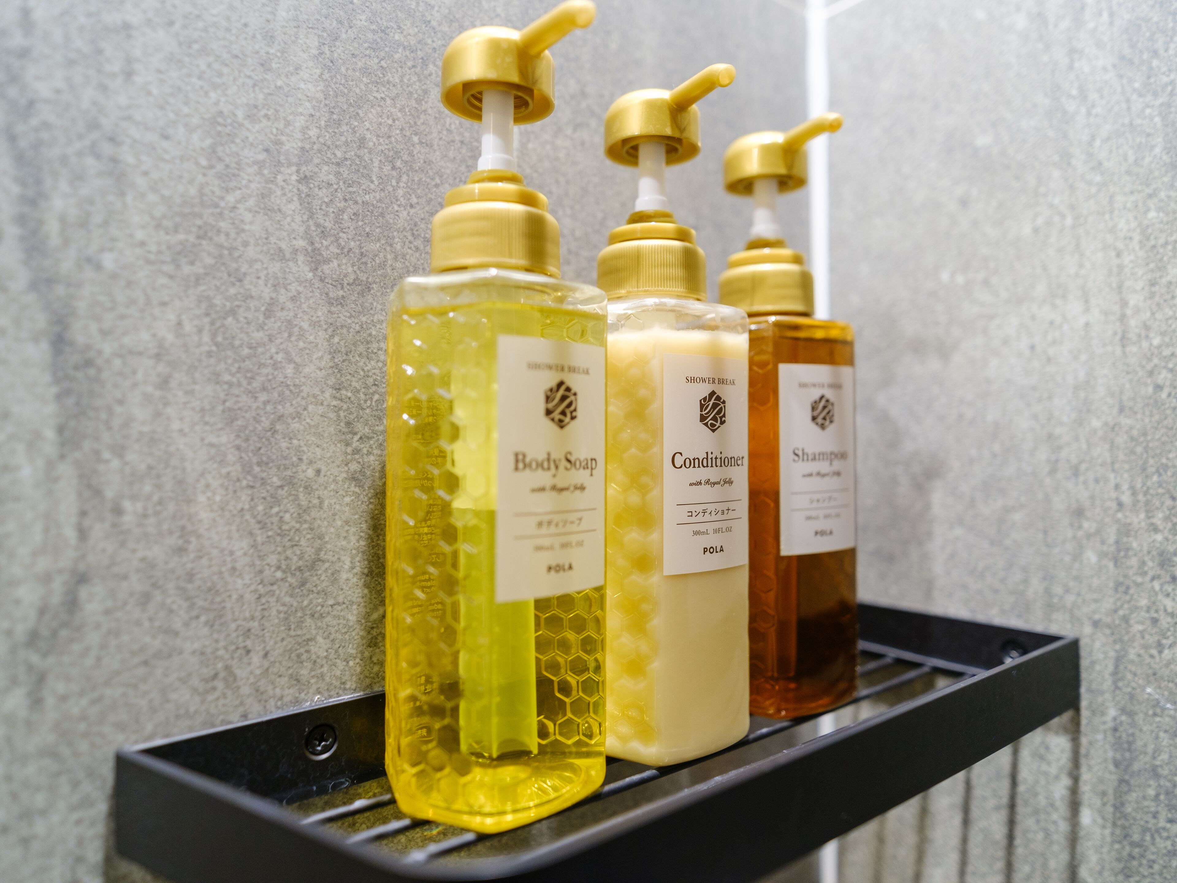 A bathroom shelf with three bottles of body care products: body soap, conditioner, and shampoo.