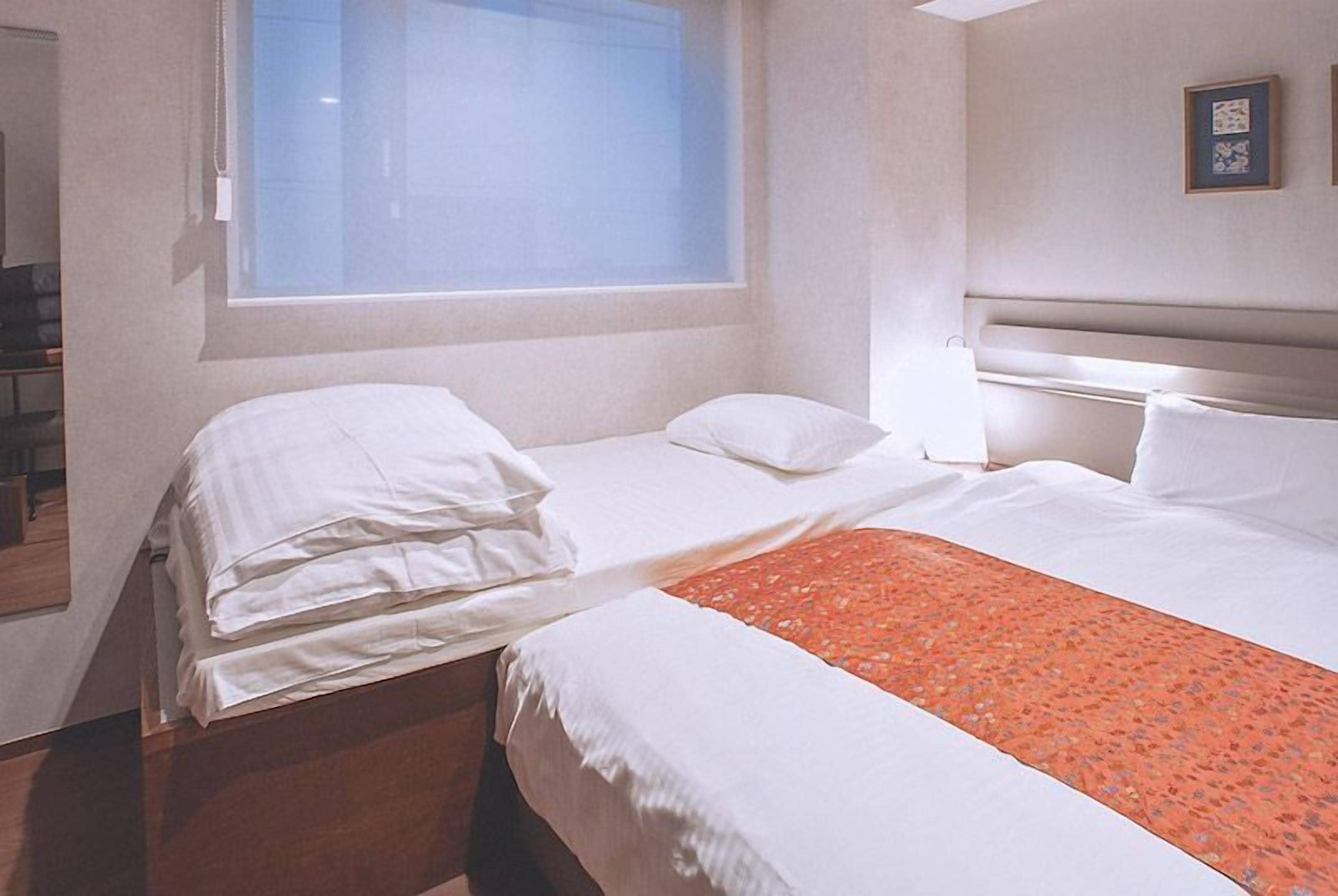 A hotel room with two beds, a window, and a framed picture on the wall.