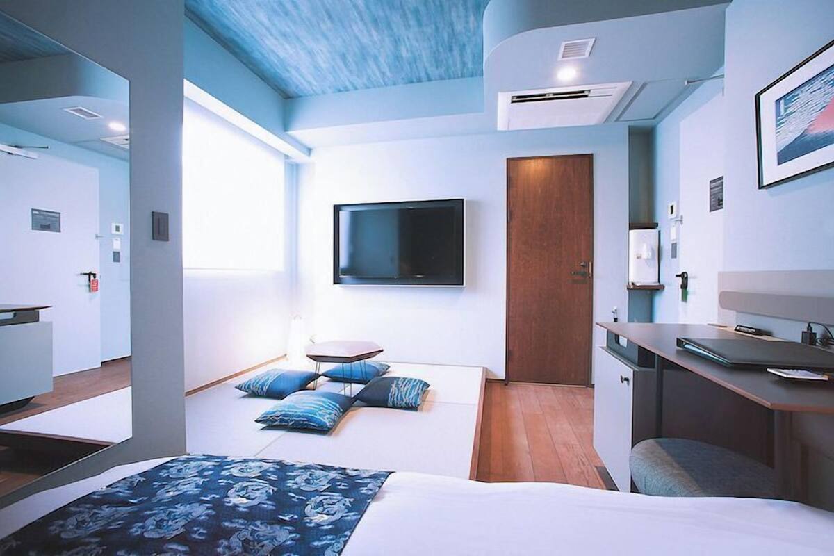 Quarto de hotel moderno com cama, escrivaninha, TV de tela plana e porta.