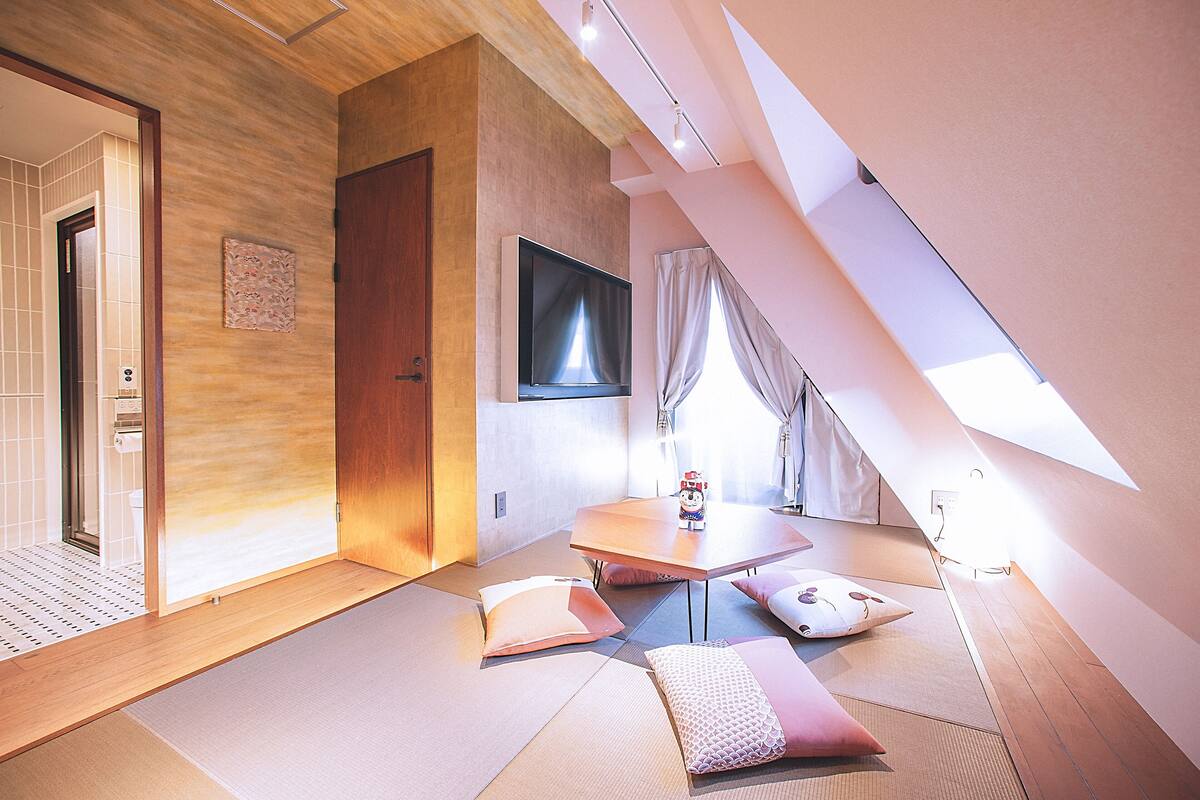 Quarto de hotel moderno com esteiras de tatame, uma TV de tela plana e porta deslizante para um banheiro.