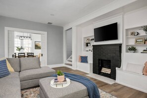 Een moderne woonkamer met een hoekbank, een open haard en een aan de muur bevestigde televisie.