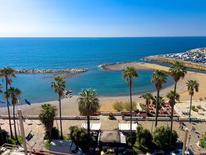 A coastal view with a beach, palm trees, and a parking area.