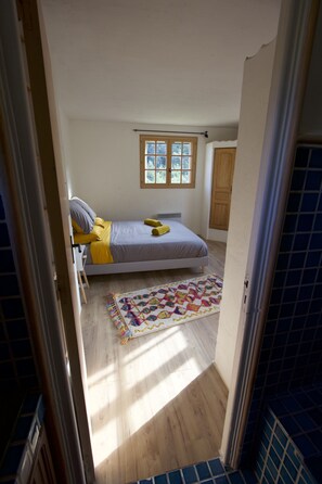 A bedroom with a bed, a window, a wooden floor, and a door.