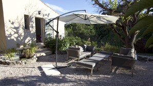Een terras met een tafel en stoelen onder een overkapping, omringd door grind en planten.