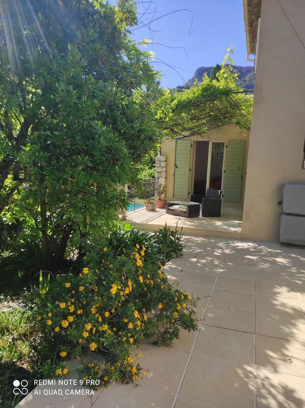 A courtyard with a tiled floor, a stone wall, and a door with green shutters.