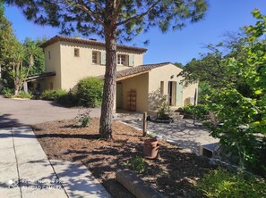 A two-story house with a tiled roof, a front porch, and a small garden area with a tree and potted plants.