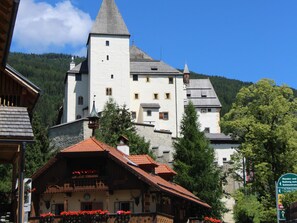 A historic building with a prominent tower, surrounded by lush greenery and traditional architecture. - Apartment with view, comfort and sauna (Mauterndorf)