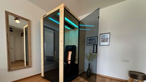 Een moderne kamer met houten vloer, een zwarte stoel, een glazen scheidingswand met houten lijst, en een vaas met groene planten.