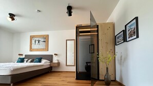 Een moderne slaapkamer met een groot bed, houten vloer, een spiegel en een vaas met bloemen.