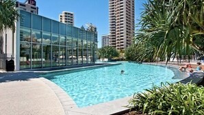 A swimming pool with a glass building in the background. - Sky Point Tower - Private Apartments (Surfers Paradise)