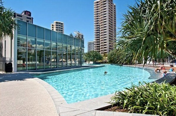 A swimming pool with a glass building in the background. - Sky Point Tower - Private Apartments (Surfers Paradise)