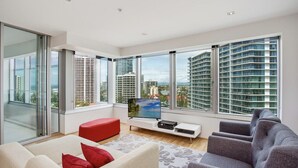 A modern living room with a large window, a flat-screen TV, a sofa, and a red ottoman. - Sky Point Tower - Private Apartments (Surfers Paradise)