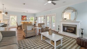 A spacious living room with a fireplace, a dining area, and a kitchen visible through an open door. - Koko Palms Home with Pool, Carriage House & Cart (Destin)
