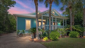 A two-story house with a porch, surrounded by palm trees and tropical plants. - Koko Palms Home with Pool, Carriage House & Cart (Destin)