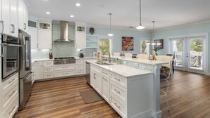 A modern kitchen with white cabinetry, a central island, and a dining area with a view to the outdoors. - Koko Palms Home with Pool, Carriage House & Cart (Destin)