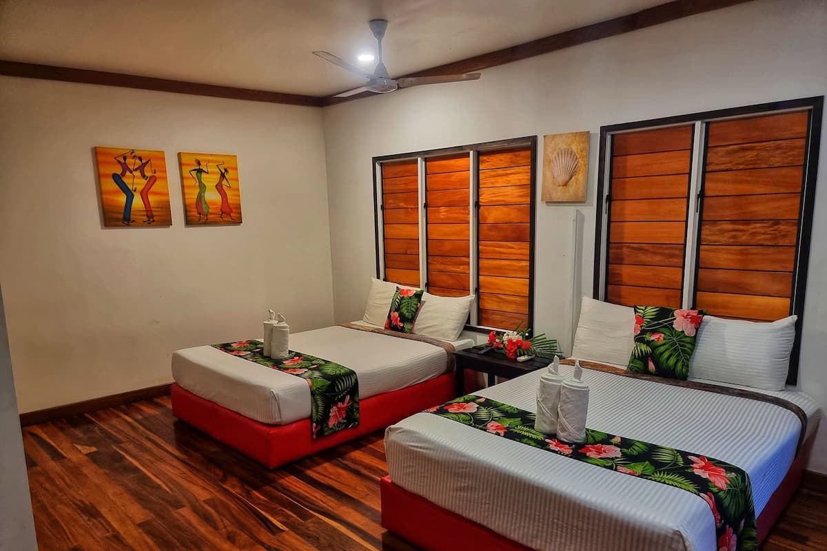 A hotel room with two beds, wooden floors, and a ceiling fan.