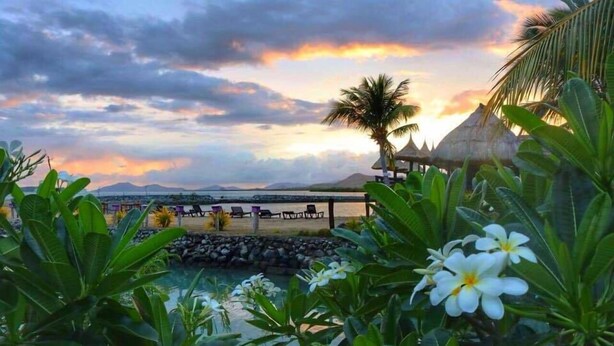 Un resort tropical con piscina, palmeras y vistas al atardecer.