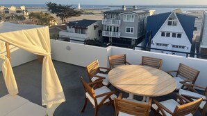 Una terraza en la azotea con una mesa y sillas de madera redondas, con vista a una playa y edificios residenciales.