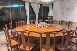 A round wooden dining table with eight chairs, surrounded by a floral centerpiece. - Danzhou Guanlan Shangpin International Hotel (Danzhou)