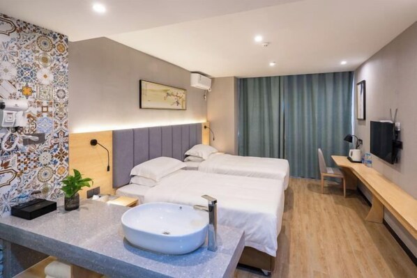 A modern hotel room with a large bed, a desk, a bathroom with a sink, and a decorative wall.