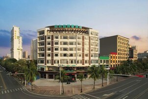 Un hotel de varios pisos con fachada curva, situado en una intersección urbana con palmeras y cielo despejado.