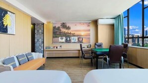 A hotel room with a sofa, a dining table with chairs, a large window with a city view, and a wall with a sunset painting. - Danzhou Guanlan Shangpin International Hotel (Danzhou)