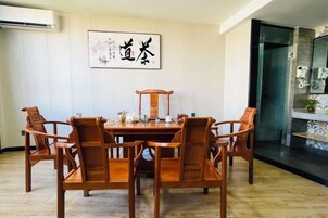 Uma sala de jantar com mesa e cadeiras de madeira, uma obra de arte emoldurada na parede e uma área de cozinha visível por uma porta aberta.