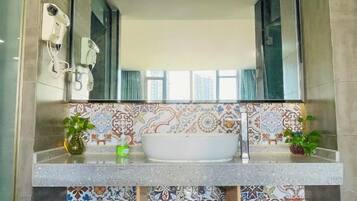 Un baño con un espejo grande, un lavamanos blanco y azulejos estampados.