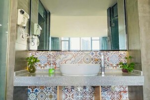 Un baño con un espejo grande, un lavamanos blanco y azulejos estampados.
