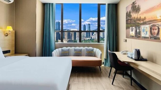 A hotel room with a bed, a sofa, a desk, a view of the cityscape, and a painting on the wall. - Danzhou Guanlan Shangpin International Hotel (Danzhou)