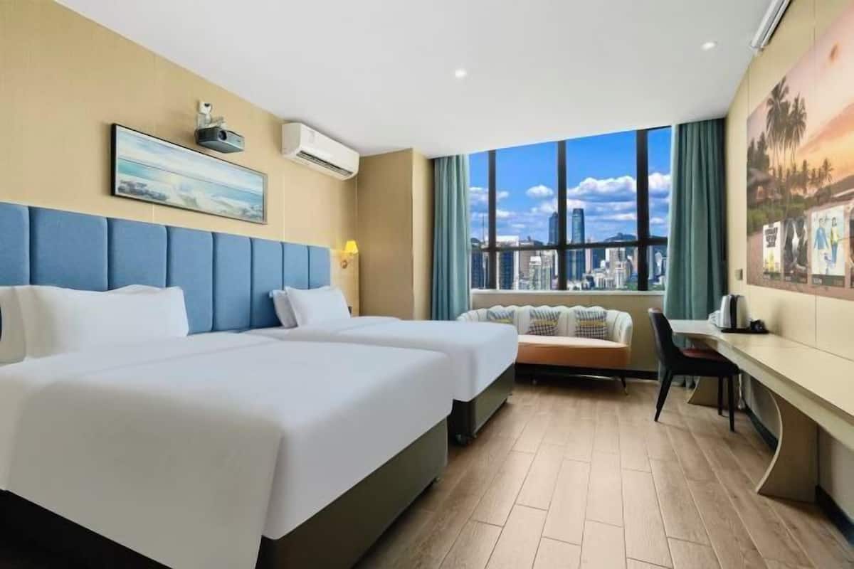 Habitación de hotel con dos camas, un escritorio, una silla, una ventana con vistas a la ciudad y un equipo de aire acondicionado.