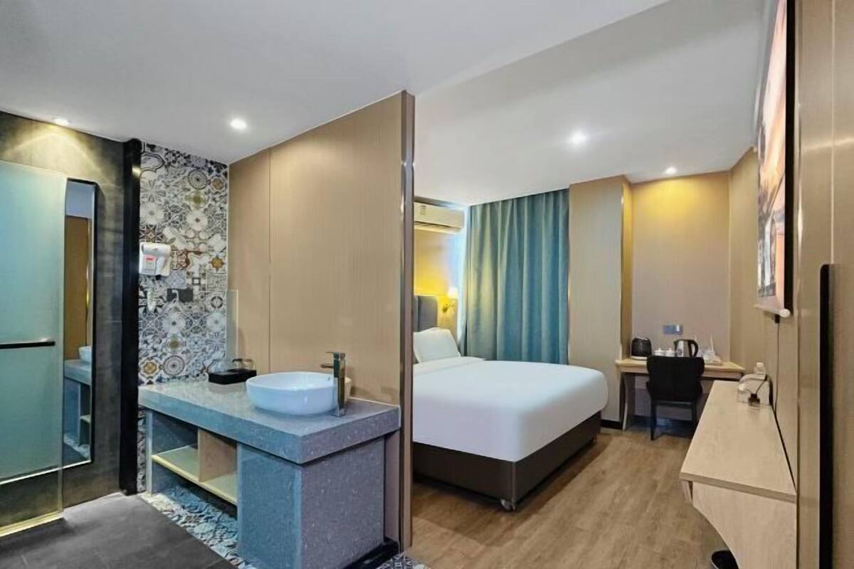Habitación de hotel con cama, escritorio, baño con lavabo y espejo.