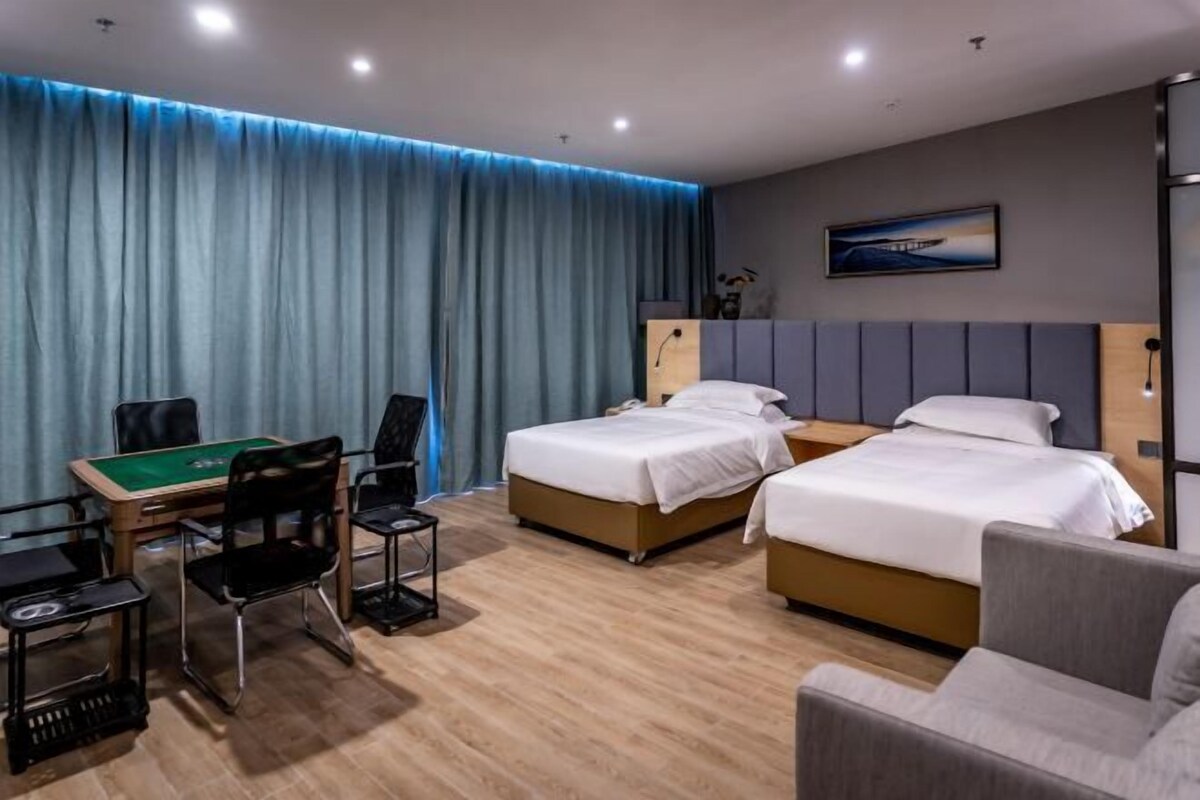 A hotel room with two beds, a desk with a green felt table, and a sofa.