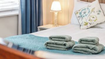 A neatly made bed with folded towels, a bedside lamp, and a floral pillow.